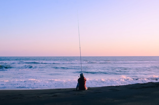 Fisher man with fishing rod on the beach at sunset