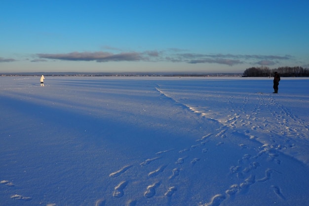 Fisherman and fisherwoman on winter fishing A man sits near a hole in a frozen lake and waits for a bite Snow on ice Bottom fishing for perch Frosty January evening Catching perch on a bloodworm