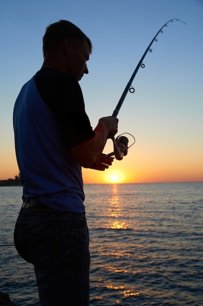 Fisherman fishes on the lake silhouette at sunset