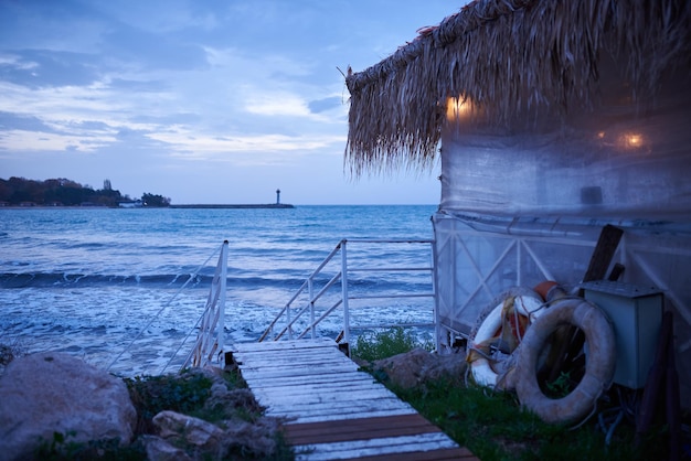 Fisherman's hut at sunrise on the sea coast with lighthouse on a horizon