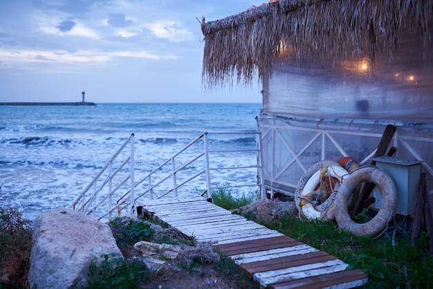 Fisherman's hut at sunrise on the sea coast with lighthouse on a horizon