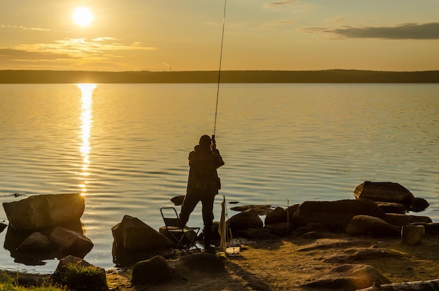 A fisherman on the shore of the lake in the early morning at sunrise.