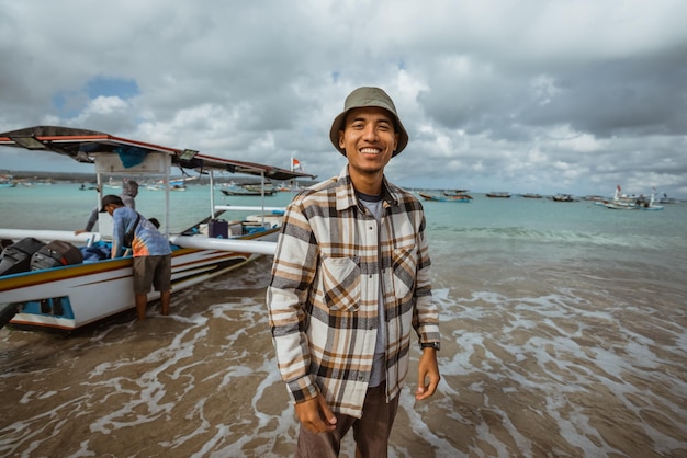 Fisherman stands with a small boat resting on the beach in the background during small waves in the