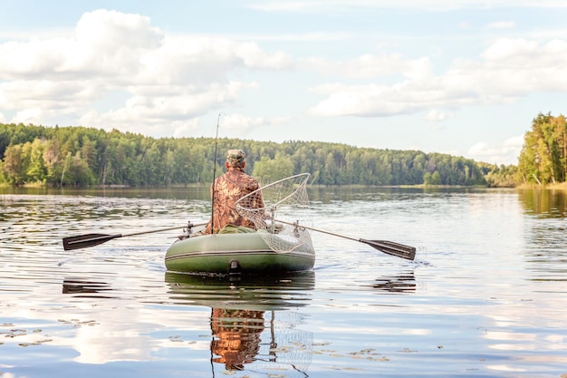 Fisherman with fishing rods is fishing in a rubber boat against background of beautiful nature and lake or river. Camping tourism relax trip active lifestyle adventure concept