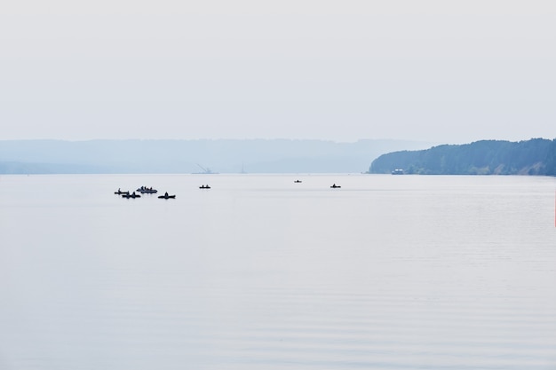 Fishermen on inflatable boats fish on a calm wide river in the morning fog