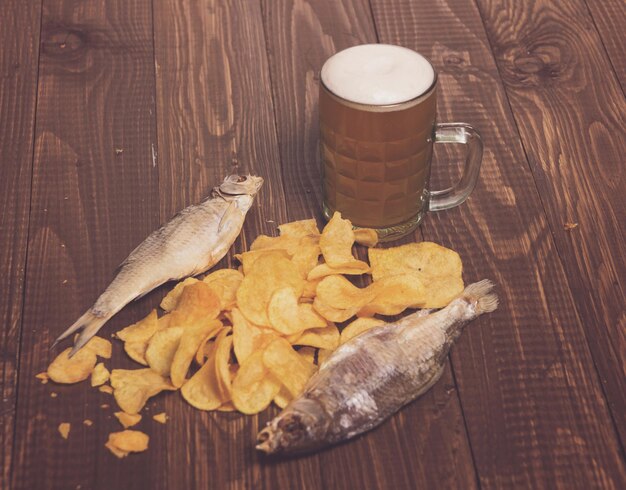 Photo fishes with frothy beer next to  diffuse chips on the wood table