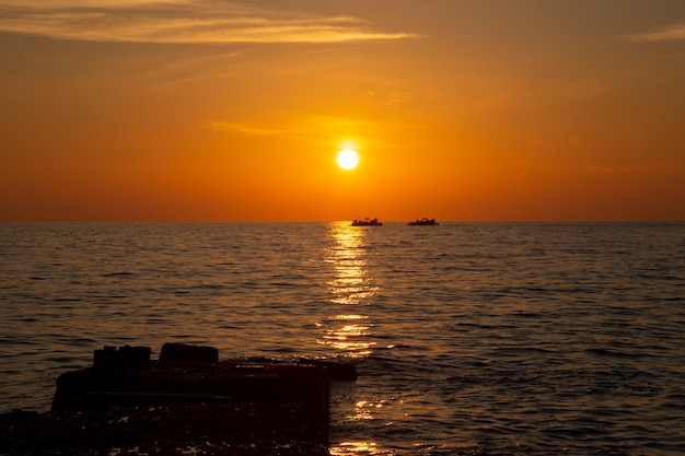 Fishing boat on the horizon, sunset on the sea. Calm sea, coral sky, evening fishing