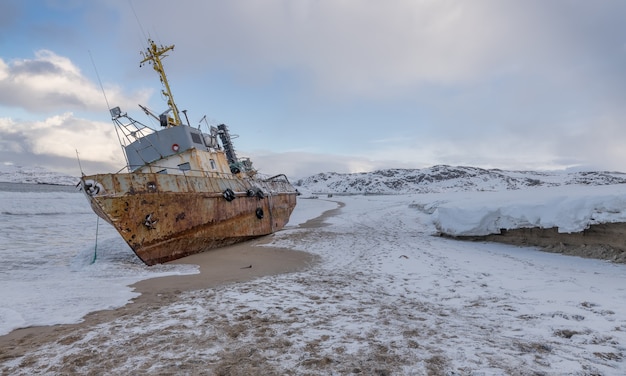 A fishing boat lying on its side, washed up by a storm on the shore of the Barents sea, the Kola Peninsula, Teriberka, Russia