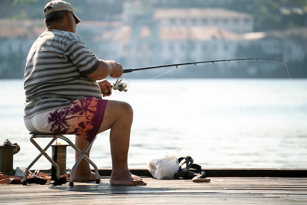 A fishing hobby, male fisherman sitting on the city river embankment and catching fish