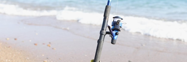 The fishing rod stands on the sand on the seashore blurry