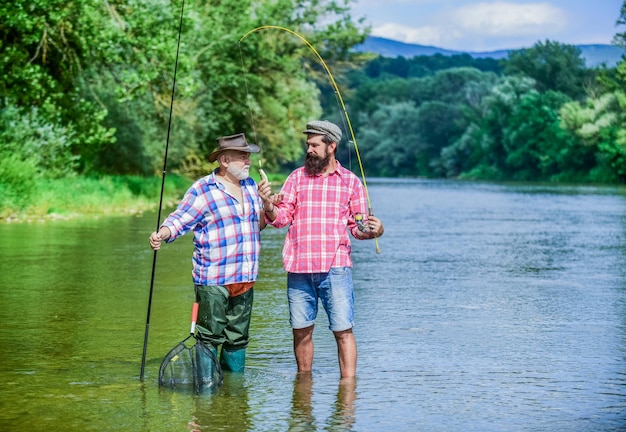 Fishing Still Keeps Us Together hobby and sport activity Trout bait two happy fisherman with fishing rods male friendship family bonding father and son fishing summer weekend men fisher