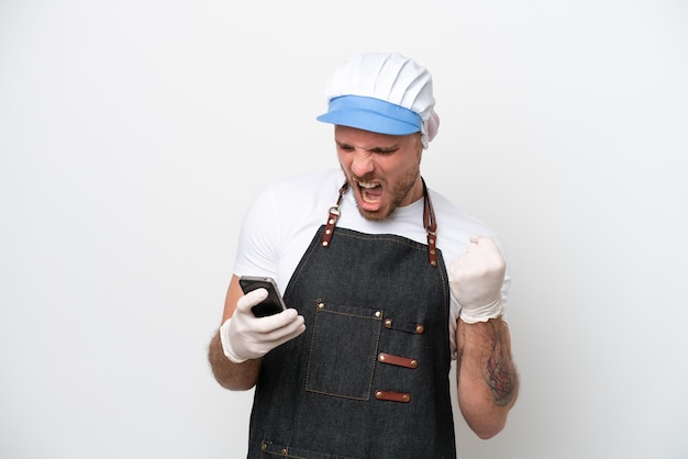 Fishmonger man wearing an apron isolated on white background with phone in victory position