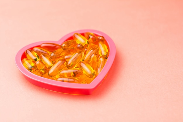 Fishoil capsules in the heart shape frame on pink with copy space.