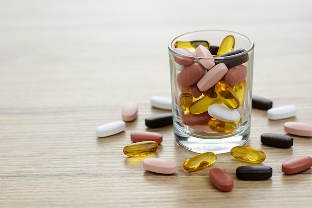 Fishoil capsules and Multivitamin supplements in the small glass on the wooden table with copy space.