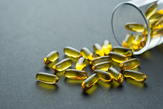 Fishoil capsules out of the small glass on black with copy space.