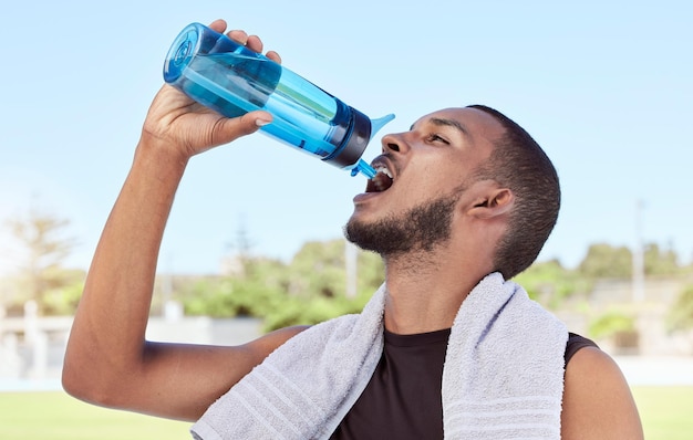 Fit active sporty man taking a break from practice to hydrate and refresh Hydrating during healthy exercise Athlete drinking and pouring water from a bottle into his mouth after workout training