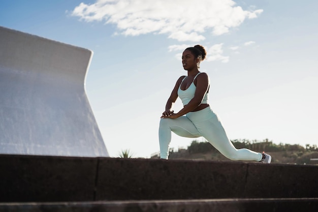 Fit african woman doing sport stretching exercise outdoor in the city - Focus on face