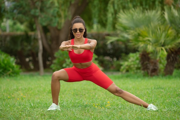 Fit black woman stretching on the grass on a sunny day.