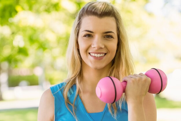 Fit blonde lifting dumbbells in the park