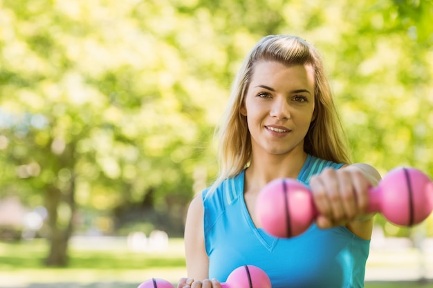 Fit blonde lifting dumbbells in the park