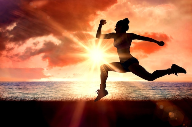 Fit brunette running and jumping against sunrise over magical sea