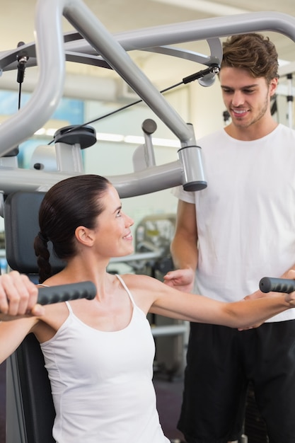 Fit brunette using weights machine for arms with trainer helping