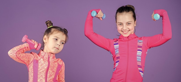 Photo fit cuties small girls enjoy fitness training with weights cute sisters doing gym fitness exercises with dumbbells little children developing physical fitness sport and fitness for kids