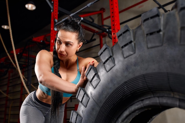 Fit female athlete working out with a huge tire turning and flipping in the gym Woman exercising with big tire