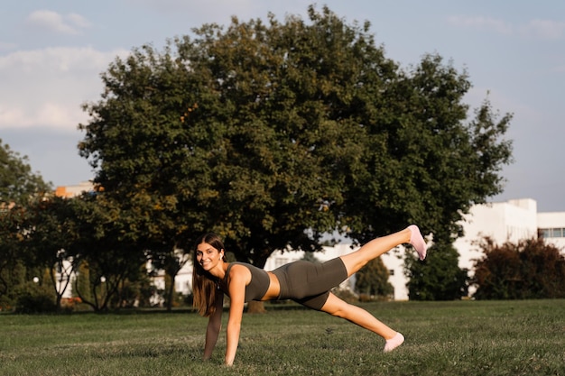 Fit girl training on green grass in the park Outdoor workout Sport lifestyle of active young woman