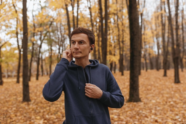 Fit male athlete using wireless earphones and listening to music during fitness workout