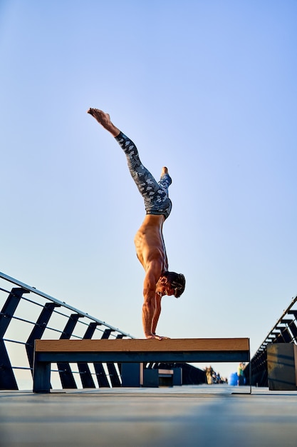 Fit man doing a hand stand while practicing yoga alone near the ocean against sky at dusk or dawn