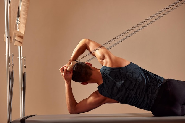 Fit man doing a lunge stretch yoga pilates exercise to strengthen and tone his muscles using a reformer in gym Health and fitness concept