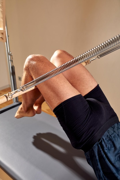 Fit man doing a lunge stretch yoga pilates exercise to strengthen and tone his muscles using a reformer in a gym