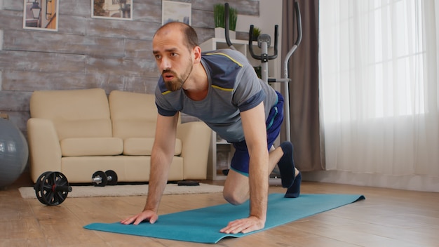 Fit man working out his core doing mountain climbers at home on yoga mat.