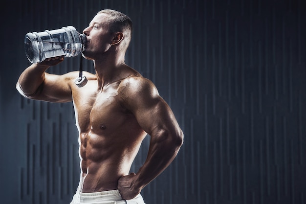 Fit man at workout in gym with shaker on dark background