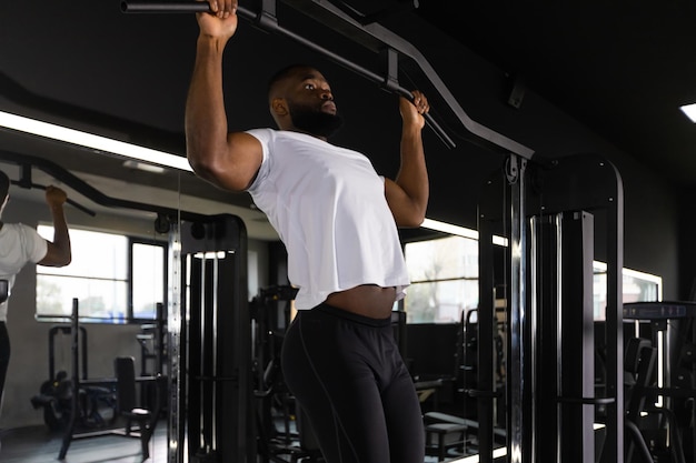 Fit and muscular african man pulling up on horizontal bar in a gym