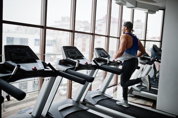 Fit and muscular arabian man running on treadmill in gym.