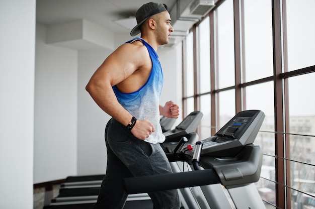 Fit and muscular arabian man running on treadmill in gym.