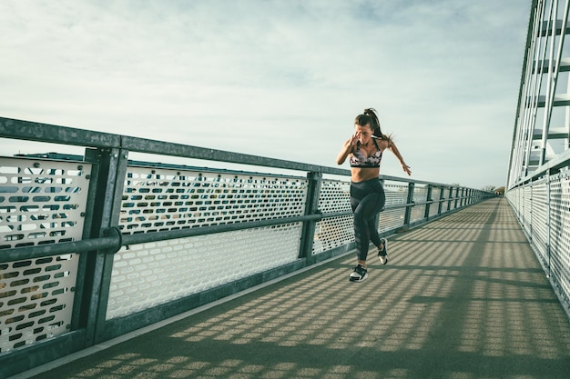 Photo fit muscular young woman runner sprinting at great speed outdoors on the river bridge.