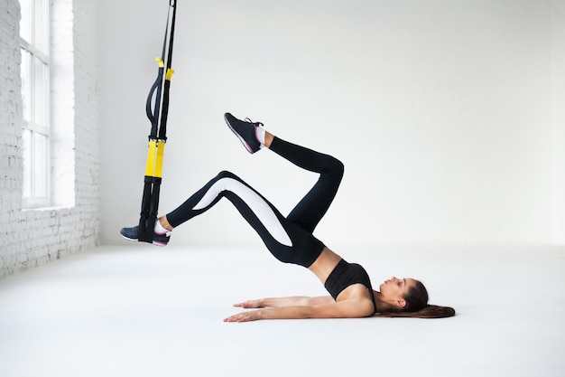 Photo fit pretty young woman doing fly yoga stretching exercises with trx fitness straps  in fitness training white gym loft classroom. sport healthy lifestyle concept. copy space.