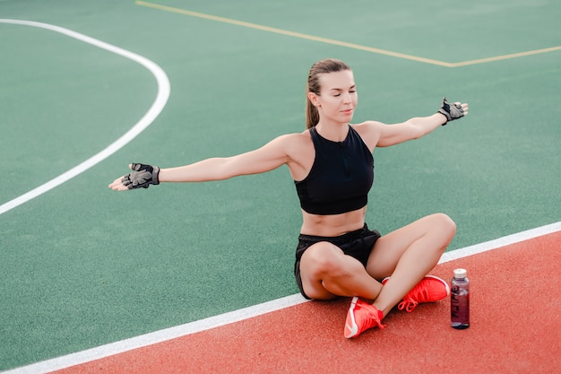 Fit sporty woman drinking water from the bottle on stadium during fitness workout