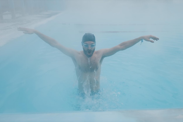 Fit swimmer male training swim in open winter swimming pool with fog Geothermal outdoor spa concept