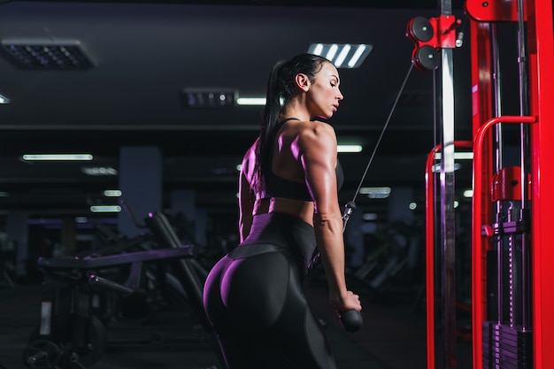 Fit well-trained woman workout triceps lifting weights in gym. Athletic sexy woman doing exercise using machine in gym 