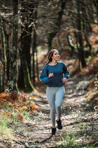 Fit woman in activewear running along trail in green forest