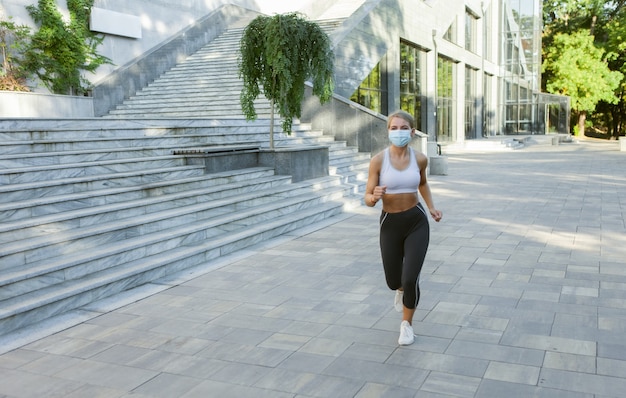 Fit woman in sportswear and medical face mask doing morning jog outdoors. Sports during covid-19 period