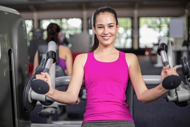 Fit woman using weight machine in gym