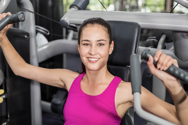 Fit woman using weight machine in gym