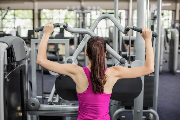 Fit woman using weight machine in gym