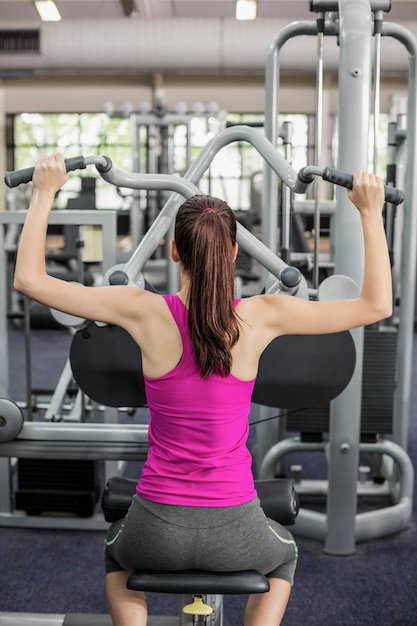 Fit woman using weight machine in gym