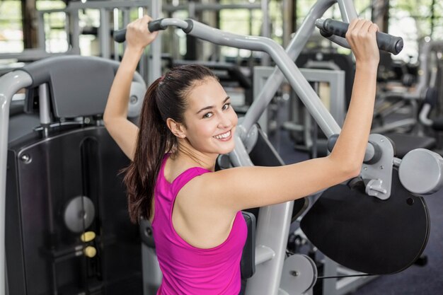 Fit woman using weight machine in gym